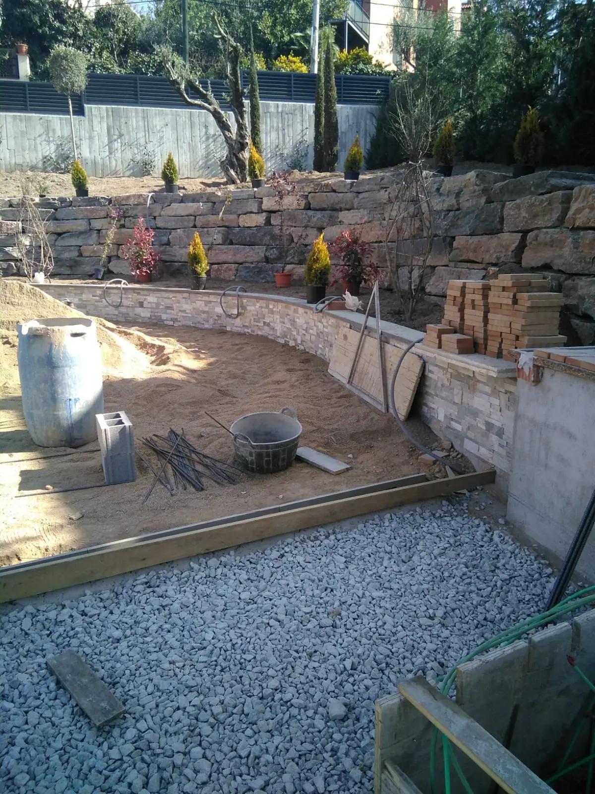 Terraza de jardín con porcelánico tipo piedra y zócalo de piedra natural.