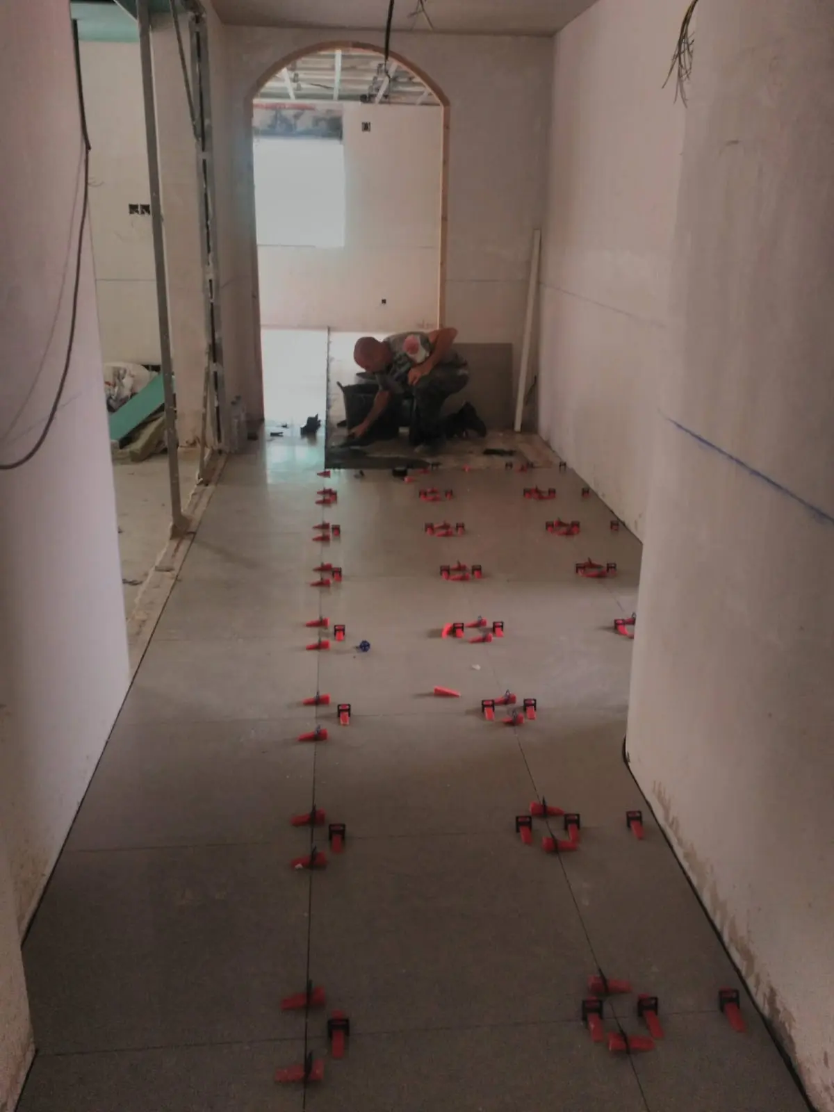 Sistema de nivelación en pasillo. Operario colocando baldosas con clips.