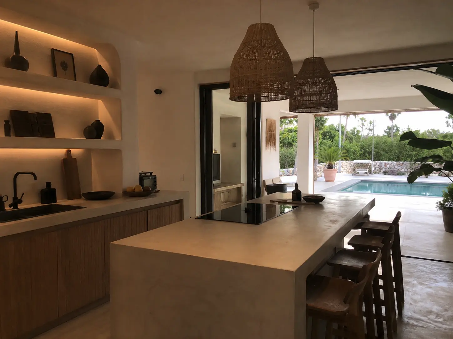 Inicio Cocina moderna reformada con isla central, estanterías iluminadas y salida al porche con piscina