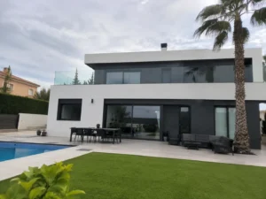 Vivienda de obra nueva moderna de dos plantas con fachada blanca, grandes ventanales, piscina y jardín