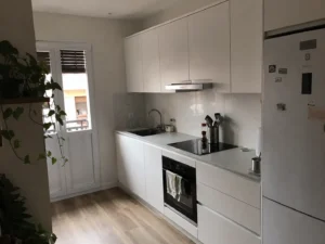 Cocina reformada en blanco y gris con vitrocerámica, horno y salida a balcón