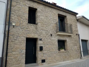 Fachada de casa de pueblo de piedra rehabilitada con balcón de forja en Tarragona